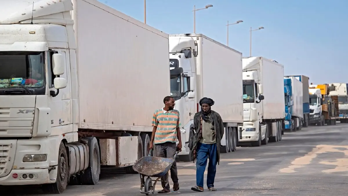 Unos hombres pasan junto a unos camiones cerca de la frontera en Guerguerat, situada en el Sáhara Occidental – PHOTO/AFP/FADEL SENNA