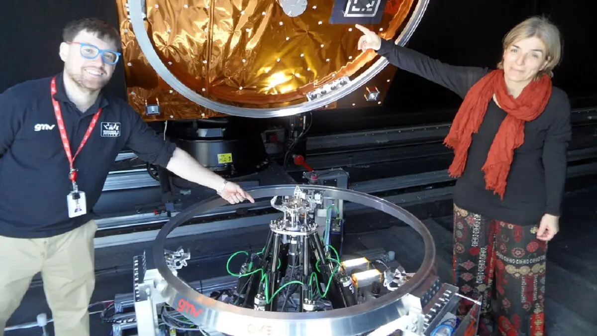 <p>La directora del segmento vuelo de GMV, Mariella Graziano, señala la sencillez del pequeño MICE bajo la estructura de un satélite. Andrés R. Reina muestra los tres dedos de CAT y los seis brazos que lo sustentan - PHOTO/JPons </p>
<p> </p>