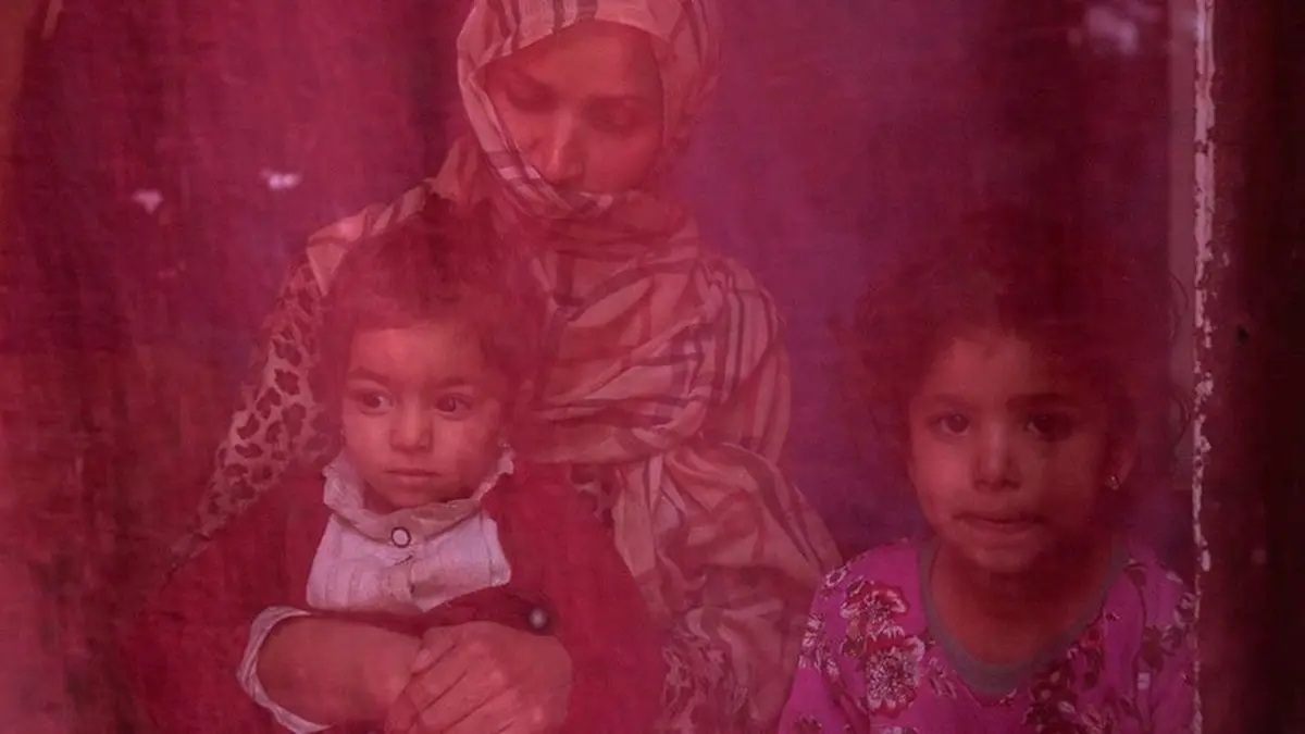 Ahora en paro, una mujer se sienta en casa con sus dos hijas -© ONU MUJERES/Sayed Habib Bidell