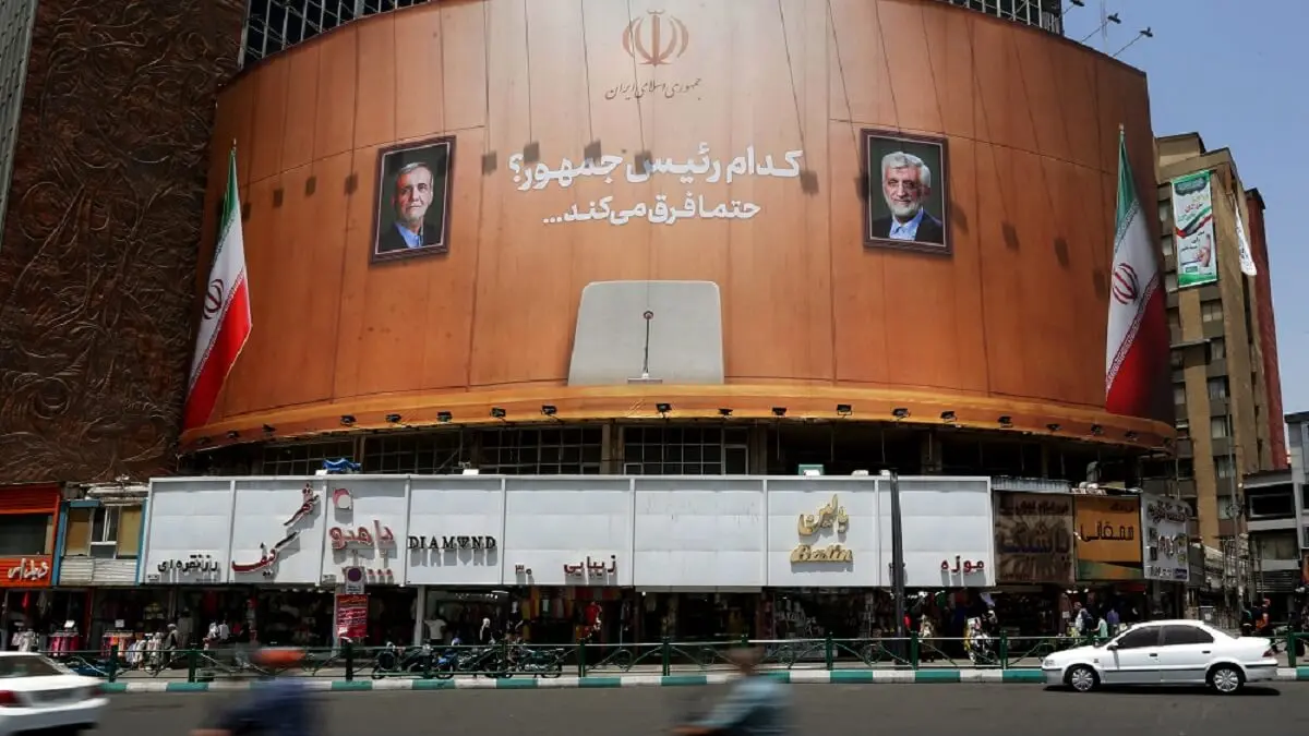 Unas motocicletas pasan junto a una enorme pancarta electoral con las imágenes del candidato reformista Massoud Pezeshkian (izq.) y del candidato ultraconservador Saeed Jalili, y la inscripción en persa “¿Qué presidente? ciertamente marca la diferencia”, en Teherán, el 4 de julio de 2024, en vísperas de la segunda vuelta de las elecciones presidenciales – PHOTO/RAHEB HOMAVANDI/AFP