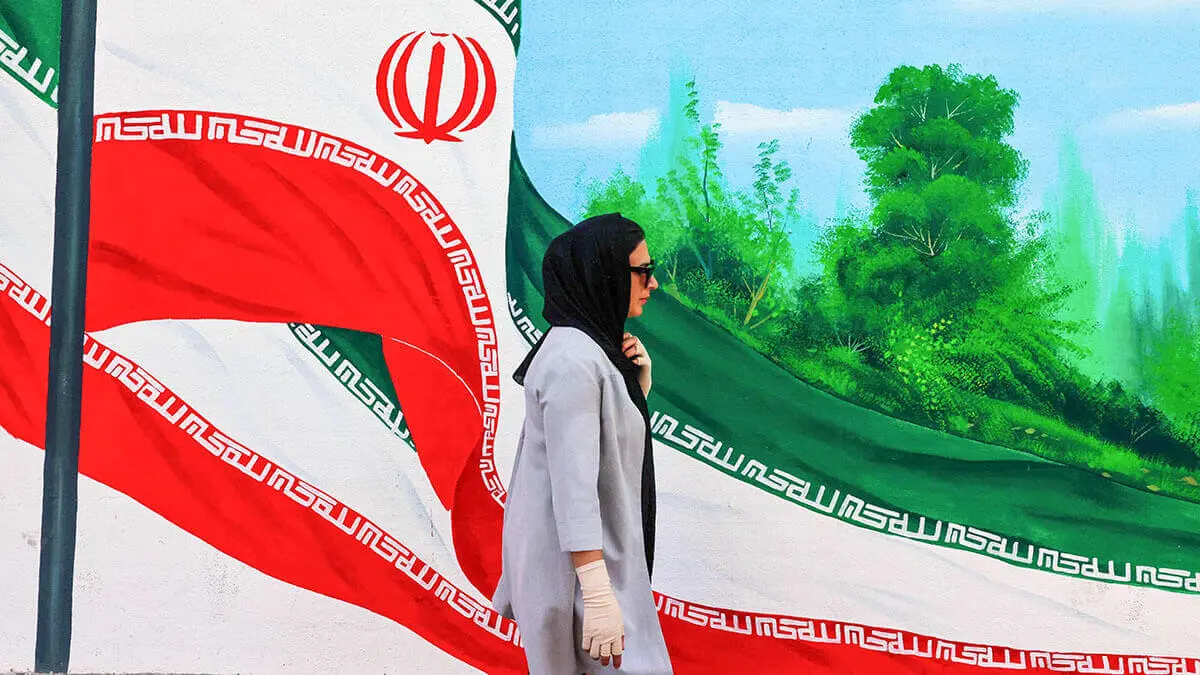 Una mujer pasa junto a un mural con banderas nacionales iraníes en una calle de Teherán el 20 de agosto de 2024 - AFP/ ATTA KENARE