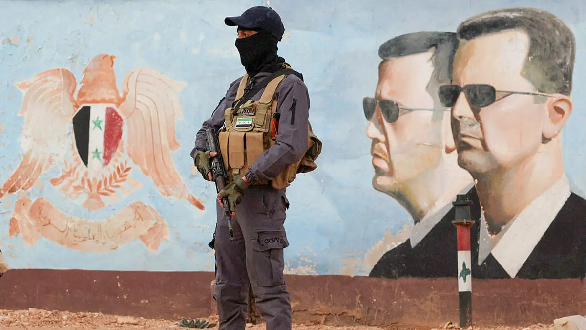 Un miembro del antiguo grupo rebelde Hayat Tahrir al-Sham hace guardia cerca de una imagen del sirio Bashar al-Assad en la sede de la cuarta división en Damasco, Siria, el 23 de enero de 2025 - REUTERS/YAMAM AL SHAAR