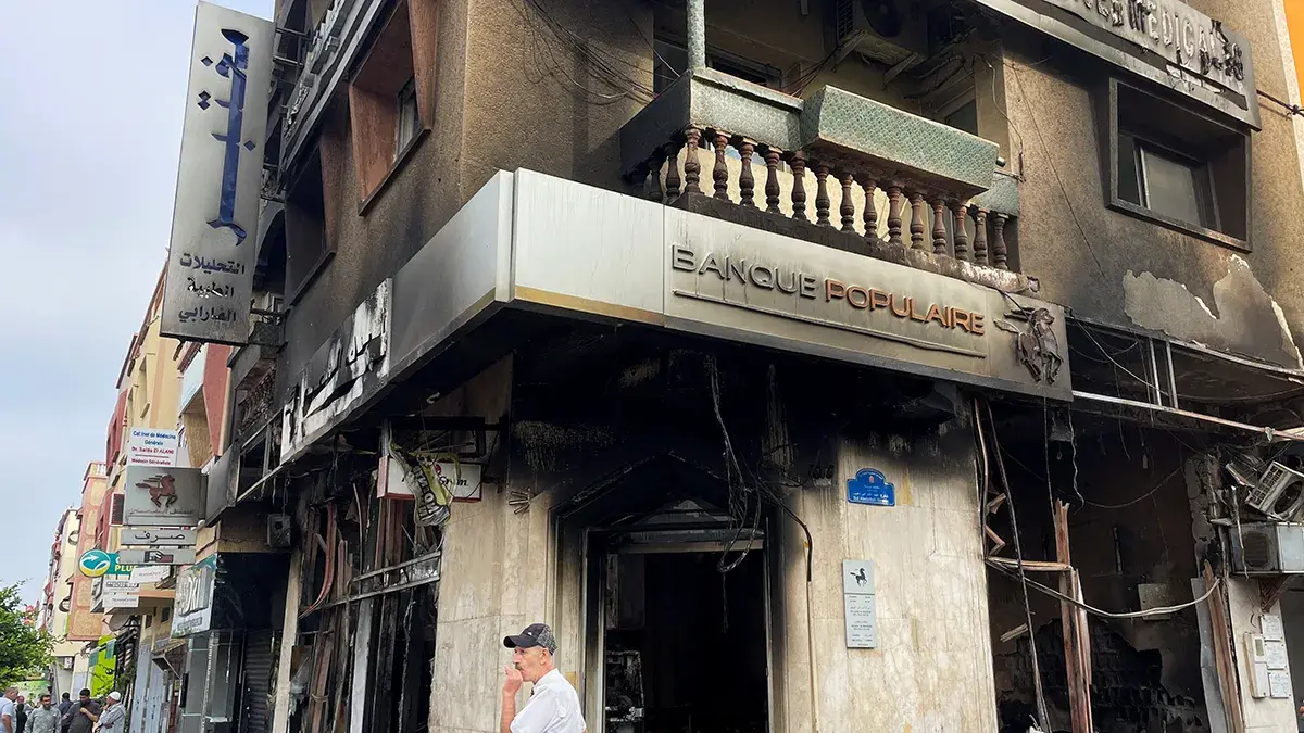 <p>Un hombre permanece junto a un edificio incendiado que albergaba un banco, tras las protestas antigubernamentales lideradas por j&oacute;venes, en Sale, Marruecos, el 2 de octubre de 2025 - REUTERS/ AHMED EL JECHTIMI&nbsp;</p>
