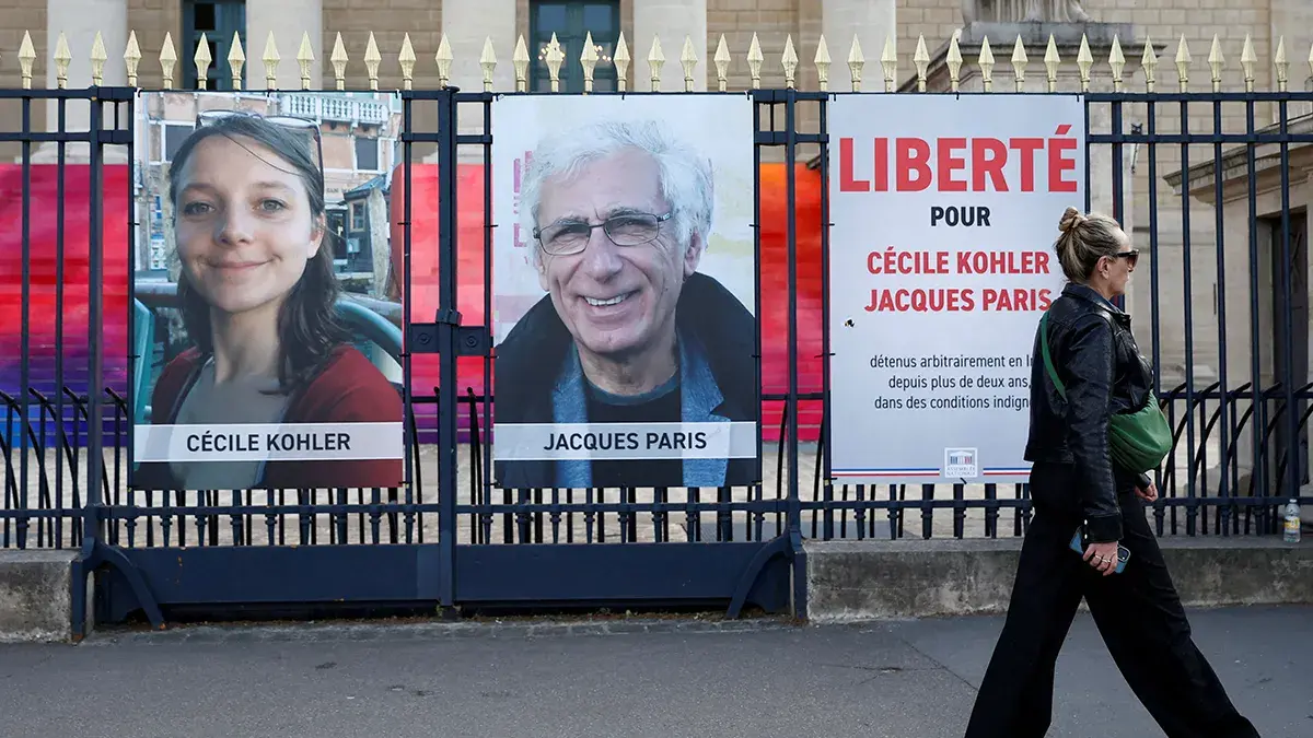 Una mujer camina frente a carteles con los retratos de los franceses Cecile Kohler y Jacques Paris, detenidos en Ir&aacute;n, durante una protesta en Par&iacute;s el 7 de mayo de 2025 que exig&iacute;a su liberaci&oacute;n tras tres a&ntilde;os de encarcelamiento&nbsp;- REUTERS/ ABDUL SABOOR