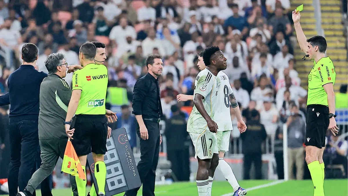 <p>El &aacute;rbitro Mateo Busquets Ferrer muestra una tarjeta amarilla a Vinicius Junior, del Real Madrid, mientras el entrenador del Atl&eacute;tico de Madrid, Diego Simeone, observa - PHOTO/ REUTERS&nbsp;</p>
