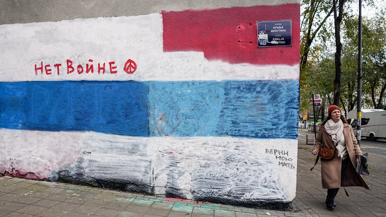 AP/DARKO VOJINOVIC - Una mujer pasa por una pared en la que solía haber un mural del presidente ruso Vladimir Putin, desde entonces pintado con una bandera blanca, azul y blanca, un símbolo de oposición a la invasión rusa de Ucrania en 2022