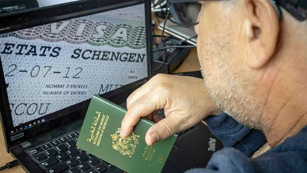 Un hombre marroquí sostiene su pasaporte frente a su ordenador que muestra un visado Schengen en la capital Rabat - AFP/FADEL SENNA