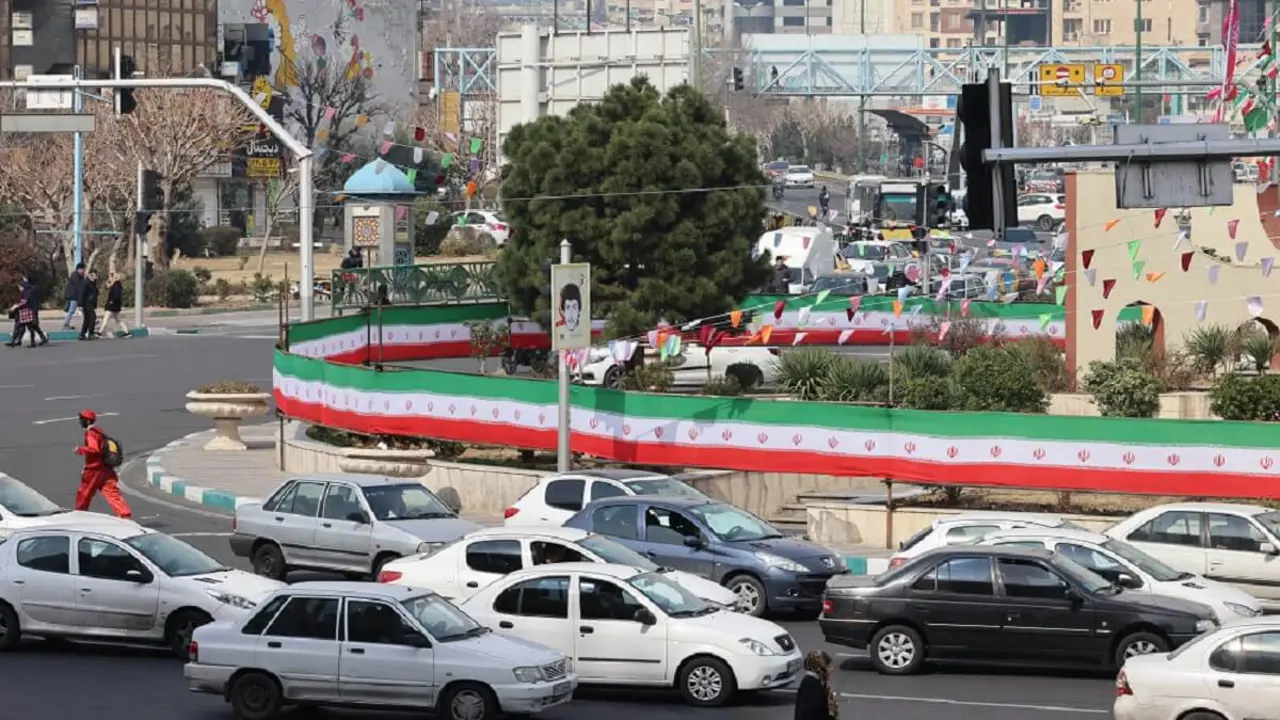 Unos coches pasan junto a un muro cubierto por una pancarta con los colores de la bandera nacional en Teherán el 3 de marzo de 2024, dos días después de que los iraníes votaran en las elecciones parlamentarias del país – PHOTO/ATTA KENARE/AFP