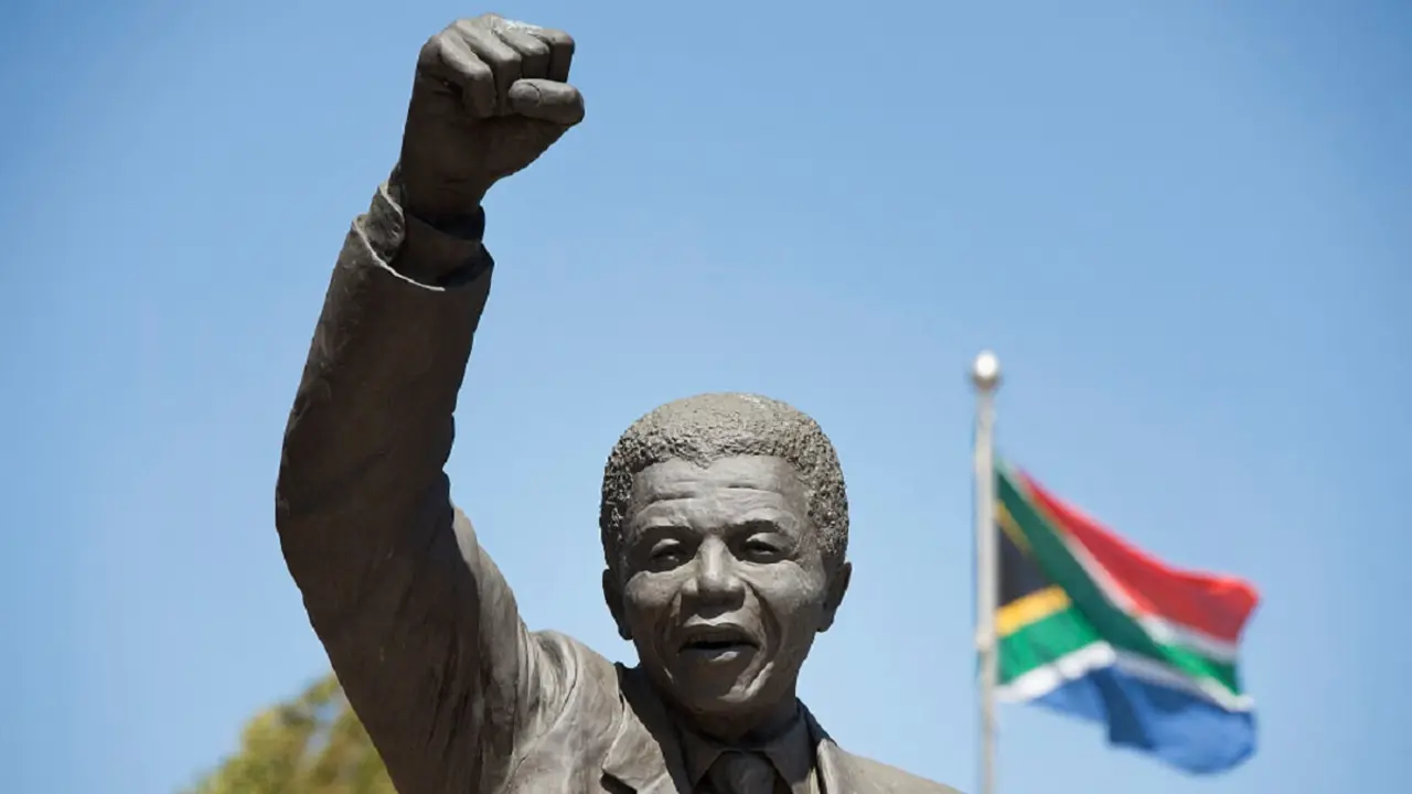 Una estatua de Nelson Mandela, revolucionario antiapartheid y expresidente de Sudáfrica, que lo representa caminando hacia la libertad con una bandera nacional sudafricana de fondo – PHOTO/RODGER BOSCH/AFP