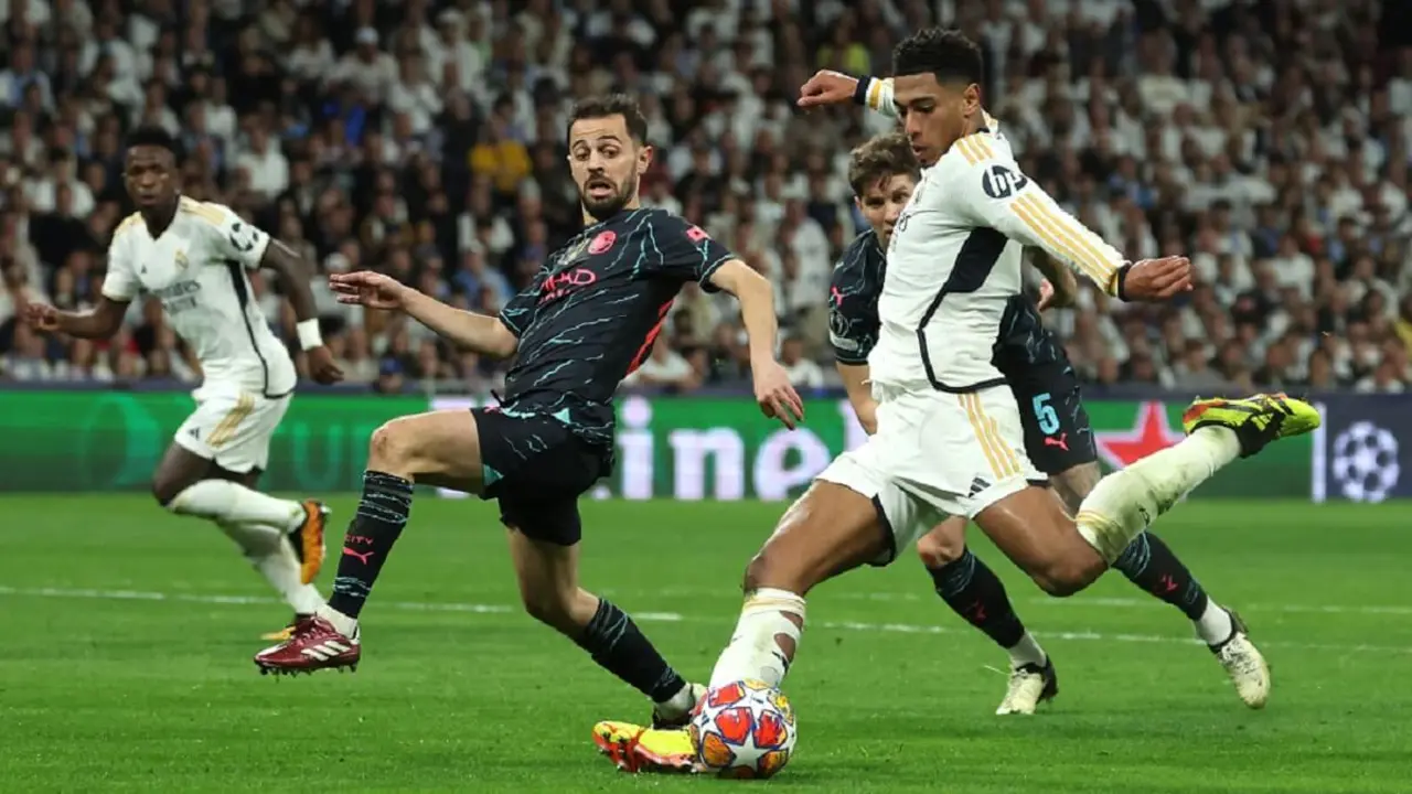 El centrocampista inglés del Real Madrid Jude Bellingham chuta el balón junto al centrocampista portugués del Manchester City Bernardo Silva y el defensa inglés John Stones durante el partido de fútbol de ida de cuartos de final de la UEFA Champions League entre el Real Madrid CF y el Manchester City en el estadio Santiago Bernabéu de Madrid el 9 de abril de 2024 – PHOTO/Pierre-Philippe MARCOU/AFP