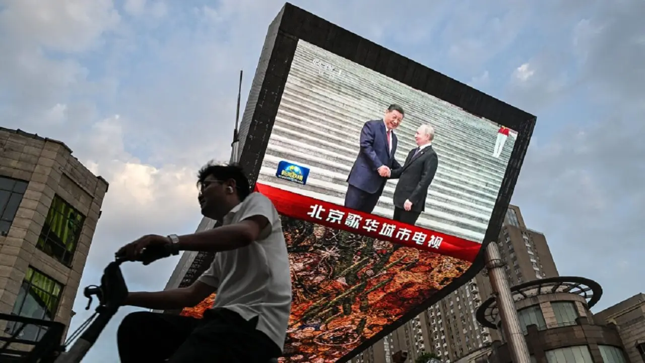 Un hombre pasa en bicicleta por delante de una pantalla gigante en un centro comercial mientras muestra un reportaje sobre la visita de Estado del presidente ruso Vladimir Putin a Pekín el 16 de mayo de 2024 – PHOTO/Héctor RETAMAL/AFP