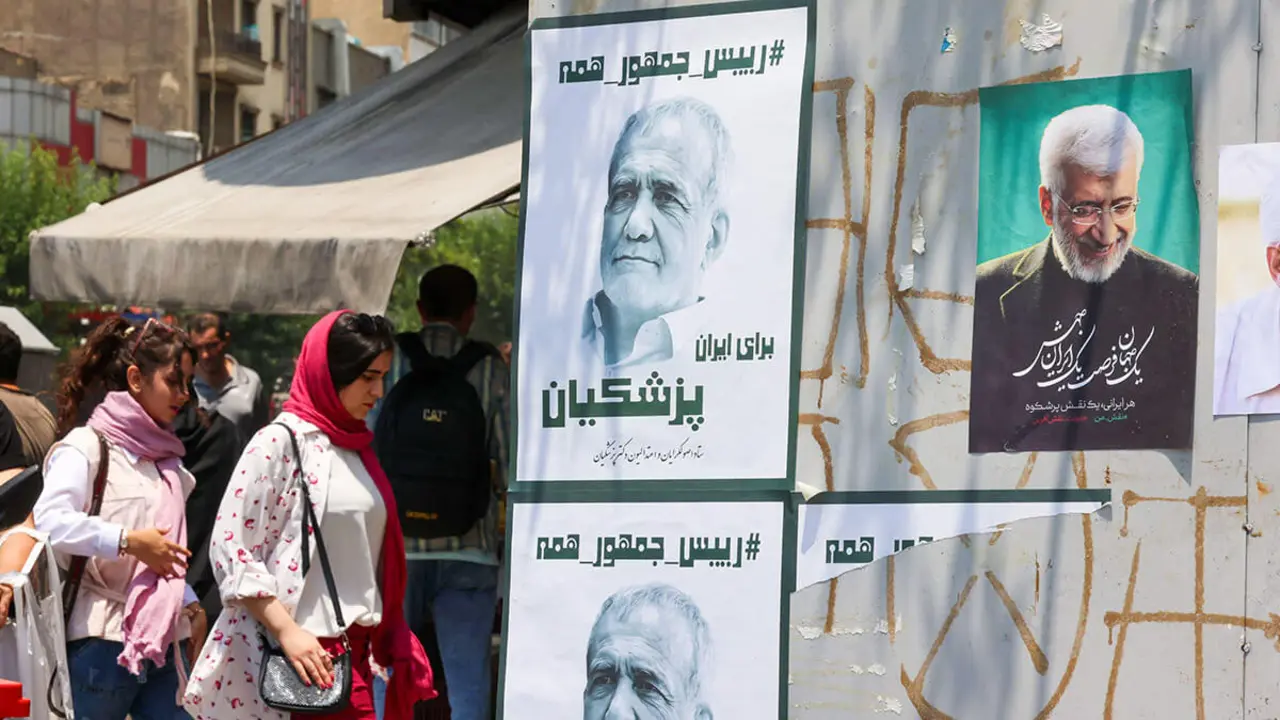 <p>Unas mujeres caminan junto a carteles electorales en Teherán el 20 de junio de 2024, antes de las elecciones del 28 de junio para sustituir al presidente Ebrahim Raisi, que murió en un accidente de helicóptero - AFP/ATTA KENARE</p>
