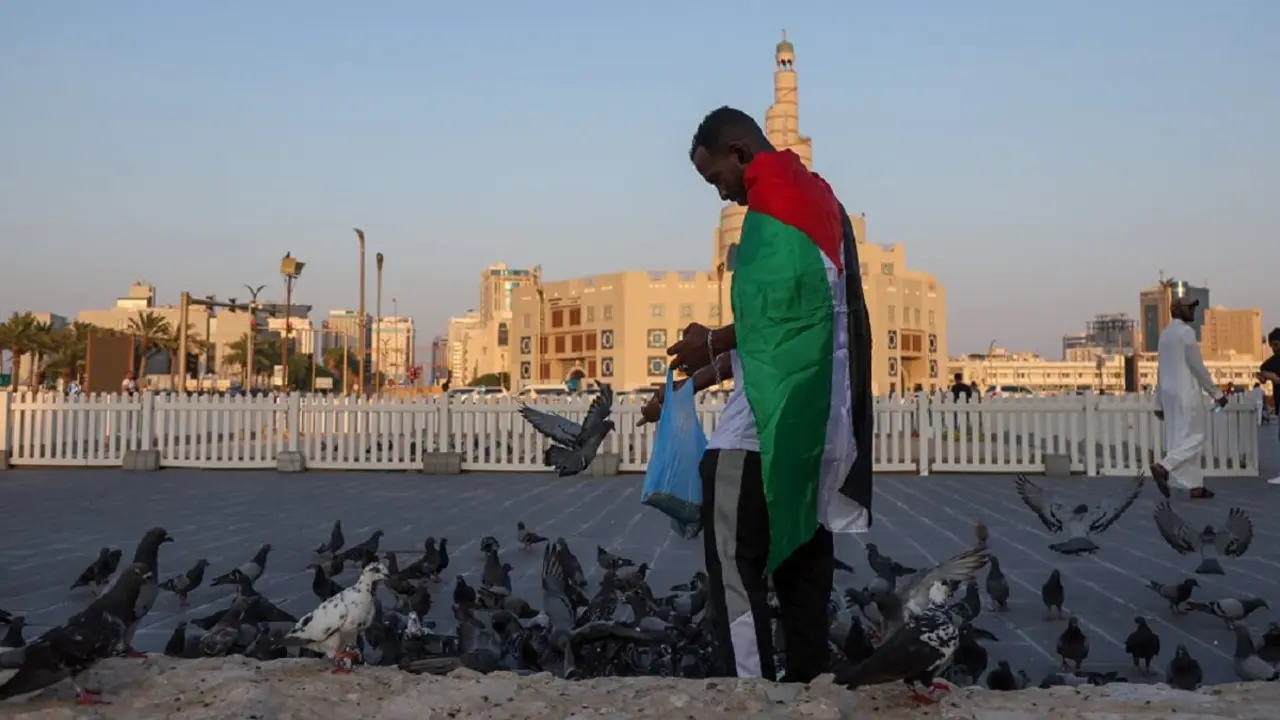 Un hombre con una bandera palestina da de comer a los pájaros cerca de la mezquita Fanar, con su minarete en espiral, en Doha, capital de Qatar, el 16 de agosto de 2024 – PHOTO/KARIM JAAFAR/AFP