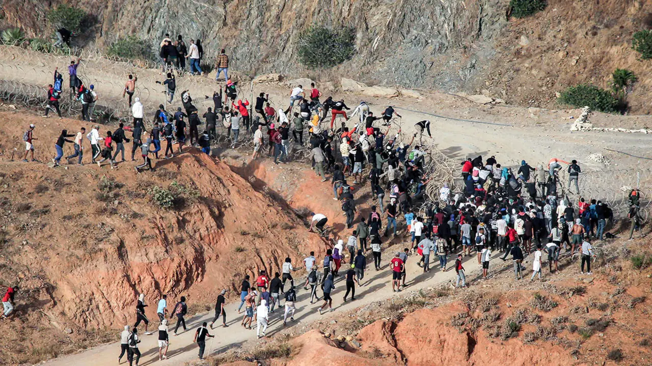<p>Migrantes asaltan una valla de alambre de púas mientras intentan cruzar la frontera terrestre con el enclave africano de España, Ceuta, cerca de Fnideq, en el norte de Marruecos, el 15 de septiembre de 2024 - PHOTO/ AFP&nbsp;</p>
