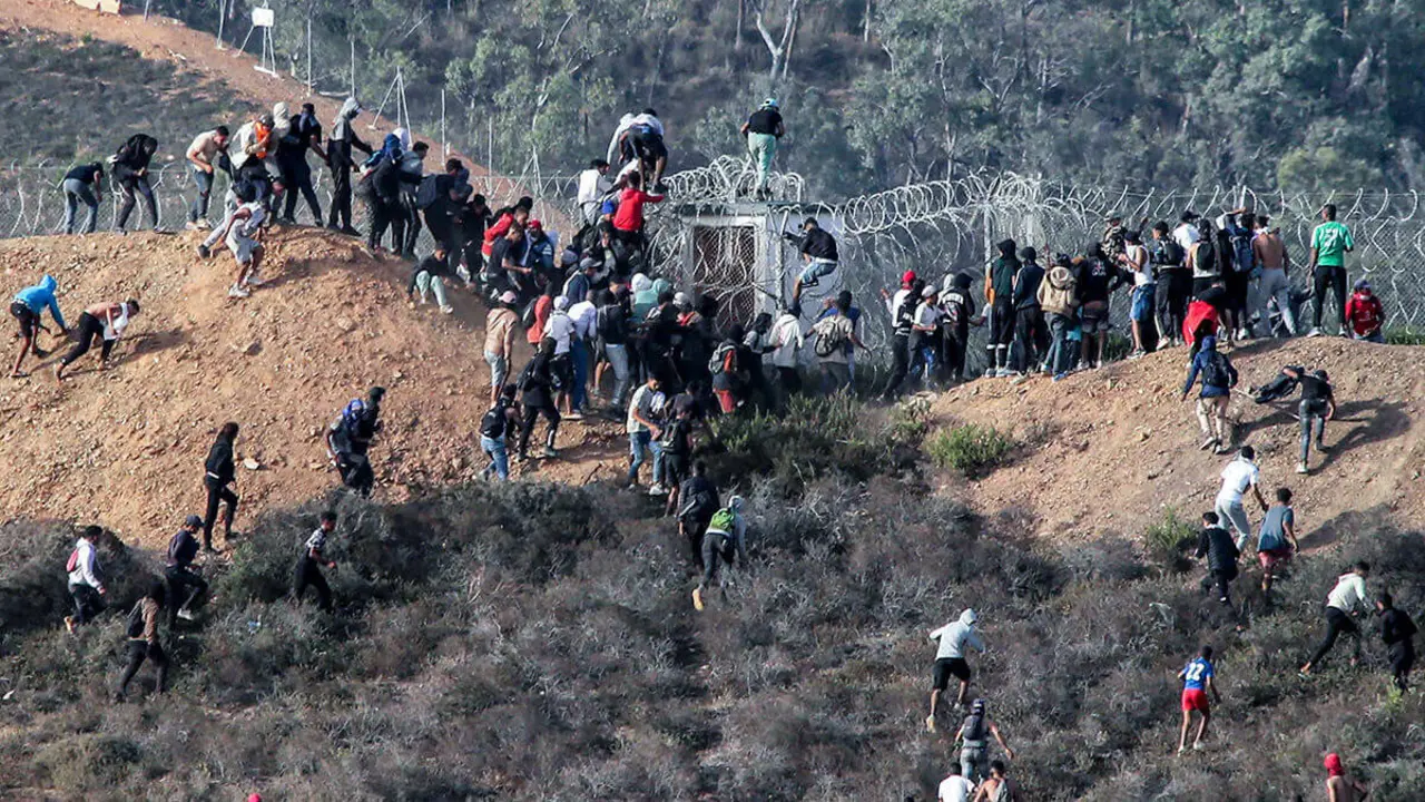 <p>Los migrantes asaltan una valla de alambre de púas mientras intentan cruzar la frontera terrestre con el enclave africano de España, Ceuta, cerca de Fnideq, en el norte de Marruecos, el 15 de septiembre de 2024 - PHOTO/ AFP<br />
&nbsp;</p>
