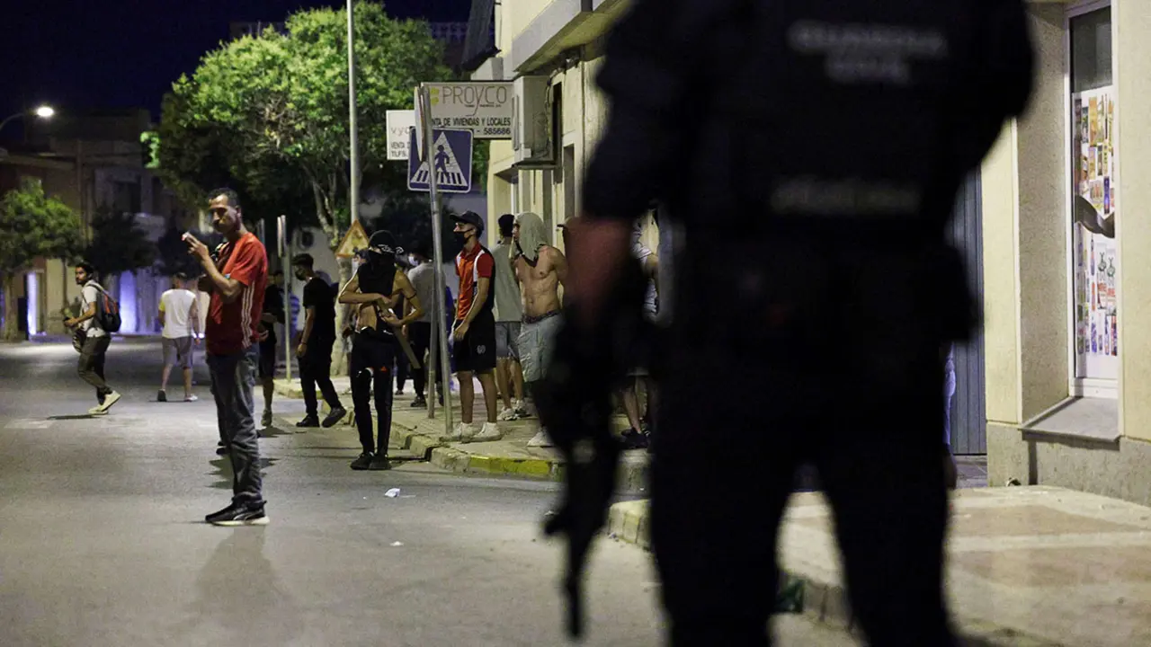 Un hombre fuma mientras la gente se reúne en una calle mientras un agente de Policía vigila, en medio de disturbios antinmigrantes tras un ataque a un anciano por parte de asaltantes desconocidos a principios de semana, en Torre Pacheco, España, el 13 de julio de 2025 - REUTERS/VIOLETA SANTOS MOURA