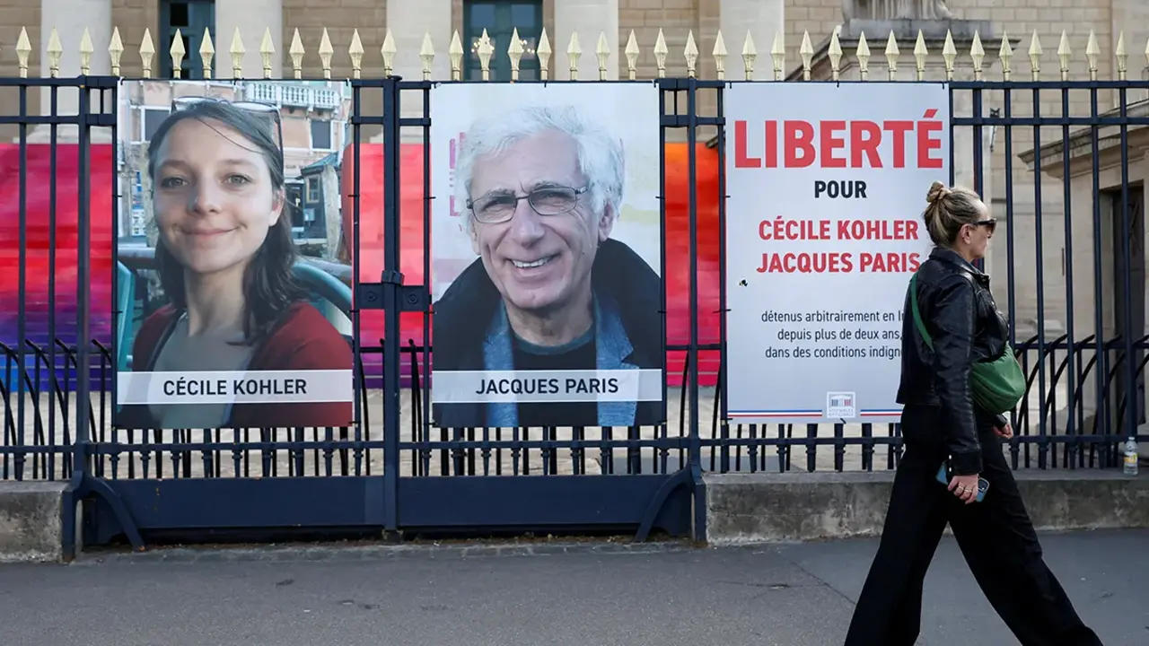 Una mujer camina frente a carteles con los retratos de los franceses Cecile Kohler y Jacques Paris, detenidos en Ir&aacute;n, durante una protesta en Par&iacute;s el 7 de mayo de 2025 que exig&iacute;a su liberaci&oacute;n tras tres a&ntilde;os de encarcelamiento&nbsp;- REUTERS/ ABDUL SABOOR
