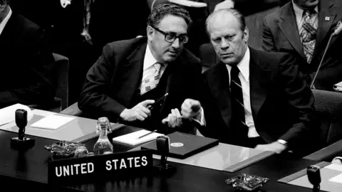 (FILES) US Secretary of State Henry Kissinger (L) speaks with US President Gerald Ford during the OTAN summit in Brussels on May 30, 1975. Former US secretary of state Henry Kissinger, a key figure of American diplomacy in the post-World War II era, died November 29, 2023 at the age of 100, his association said. (Photo by AFP)