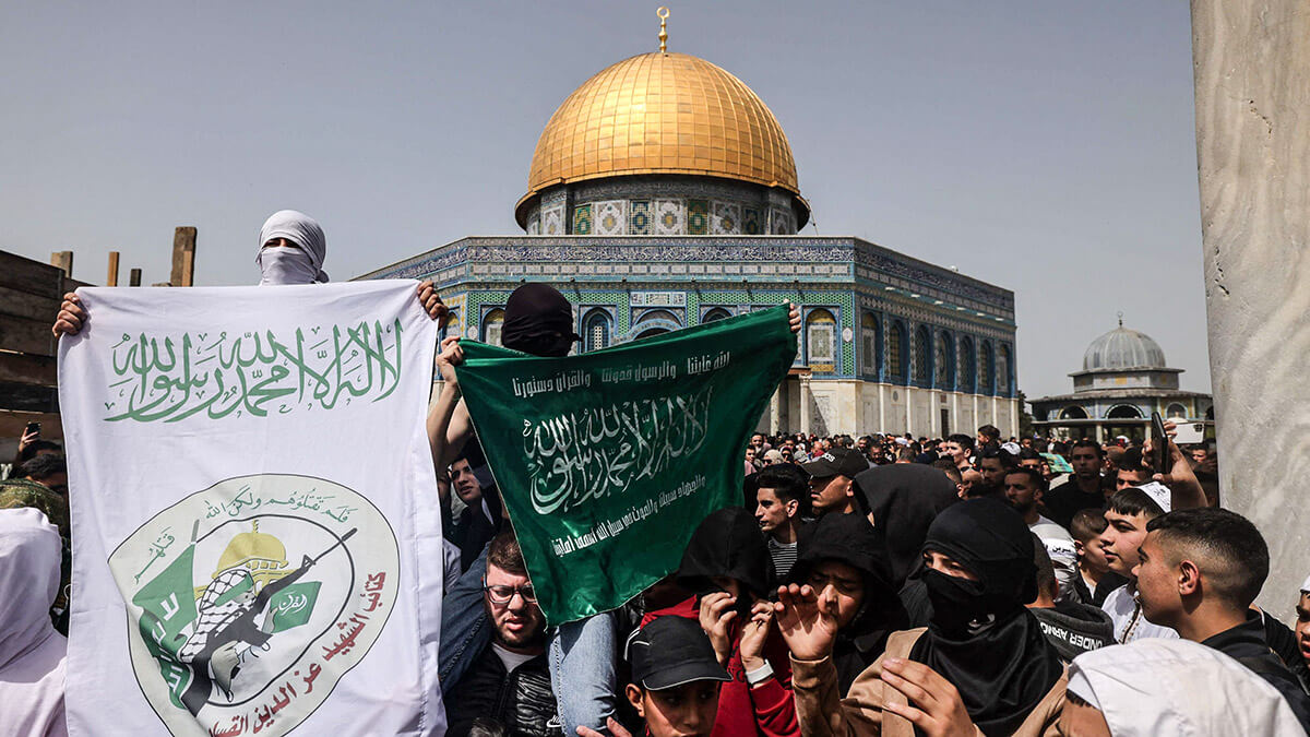 Varias personas levantan una pancarta (izq.) con el logotipo de las Brigadas Ezzedine al-Qassam, brazo militar del movimiento palestino Hamás, tras la primera oración del mediodía del viernes del mes de ayuno islámico de Ramadán, frente al santuario de la Cúpula de la Roca, en el complejo de la mezquita de Al-Aqsa, en Jerusalén, el 24 de marzo de 2023
AFP/AHMAD GHARABL