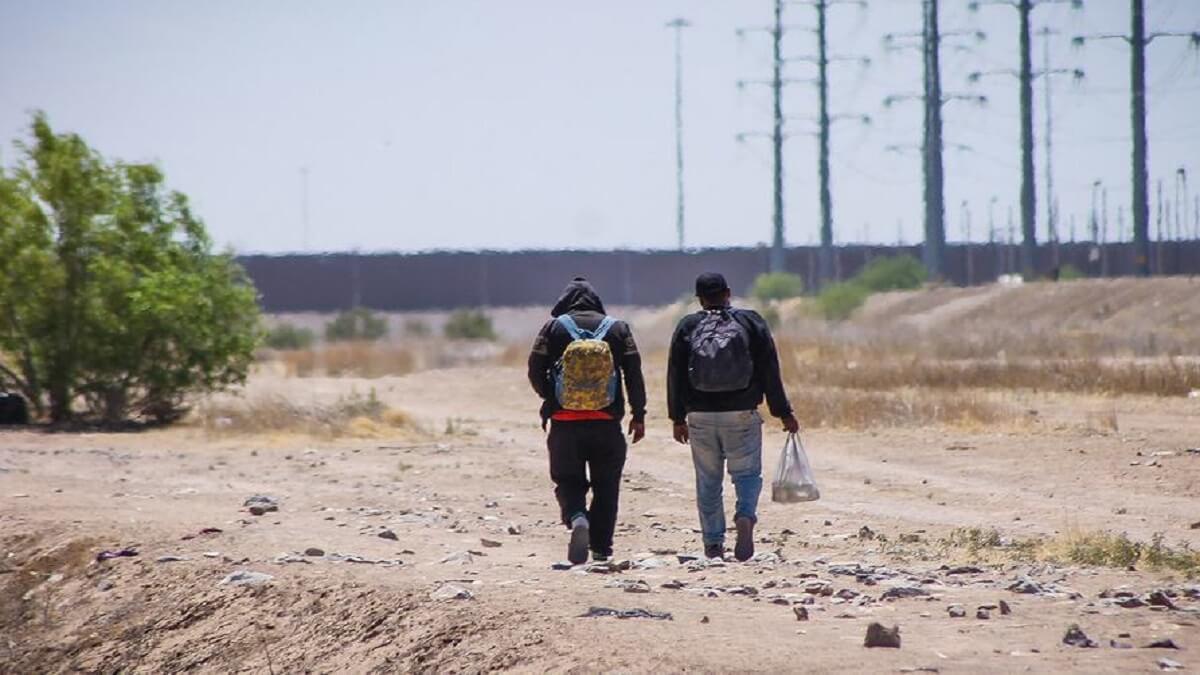 Dos hombres caminan junto al muro fronterizo que divide México de Estados Unidos - © OIM/Camilo Cruz