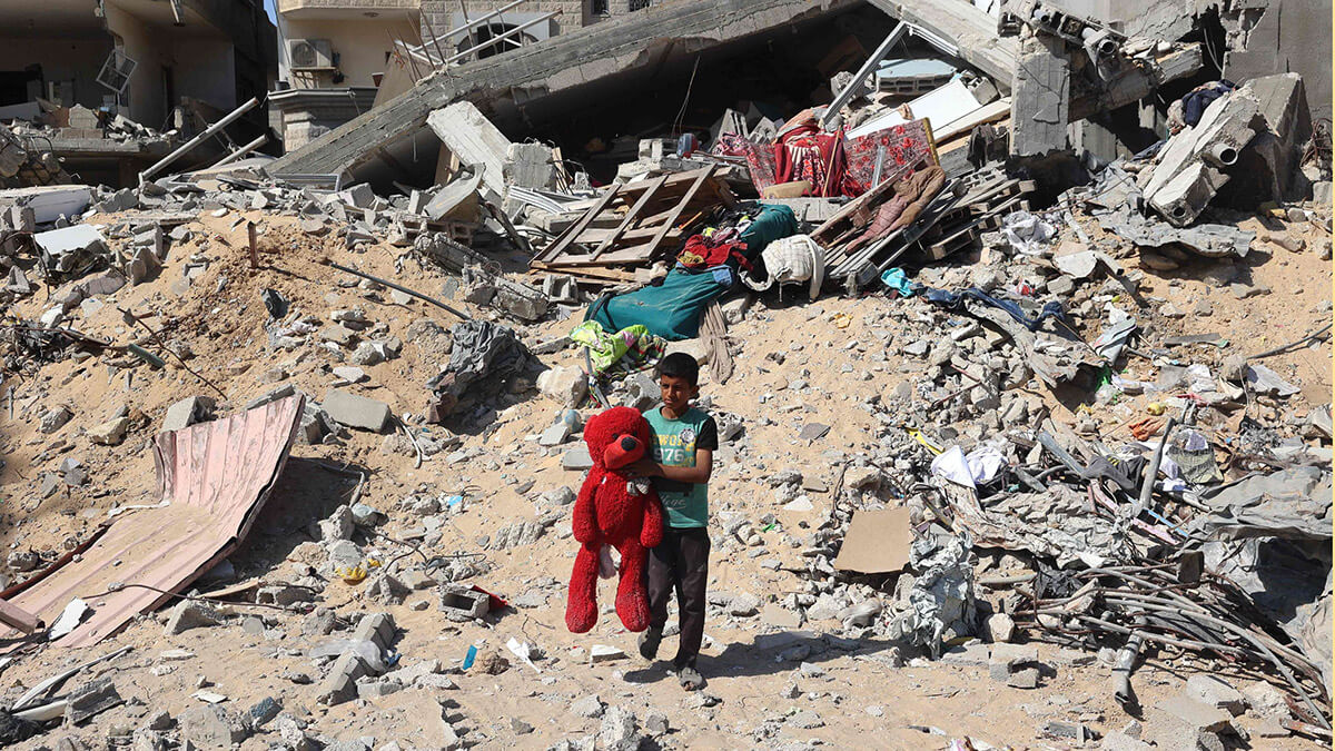 Un niño palestino camina con un oso de peluche recuperado de entre los escombros de un edificio destruido tras un bombardeo israelí en Yan Yunis - AFP/EYAD BABA