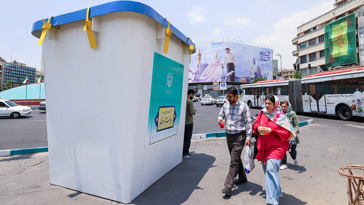 <p>Varias personas pasan junto a una réplica de una urna electoral instalada en una calle de Teherán el 20 de junio de 2024, antes de las elecciones del 28 de junio - AFP/ATTA KENARE</p>