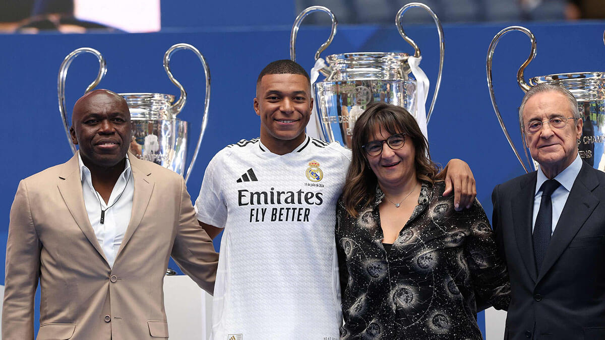 <p>El delantero francés Kylian Mbappé (2.a izq.) posa con sus padres Wilfrid Mbappé (izq.) y Fayza Lamari (2.a der.) y el presidente del Real Madrid, Florentino Pérez, durante su primera aparición como jugador del Real Madrid en el Estadio Santiago Bernabéu de Madrid el 16 de julio de 2024 - AFP/PIERRE-PHILIPPE MARCOU </p>
