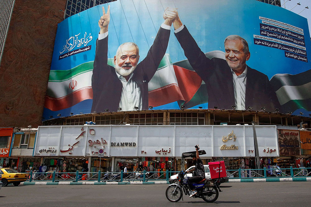 <p>Un hombre hace el signo de la victoria mientras va en bicicleta frente a un enorme cartel que representa al presidente iraní Masoud Pezeshkian (derecha) y al líder asesinado del grupo palestino Hamás Ismail Haniyeh en la plaza Valiasr de Teherán el 8 de agosto de 2024 - PHOTO/AFP </p>