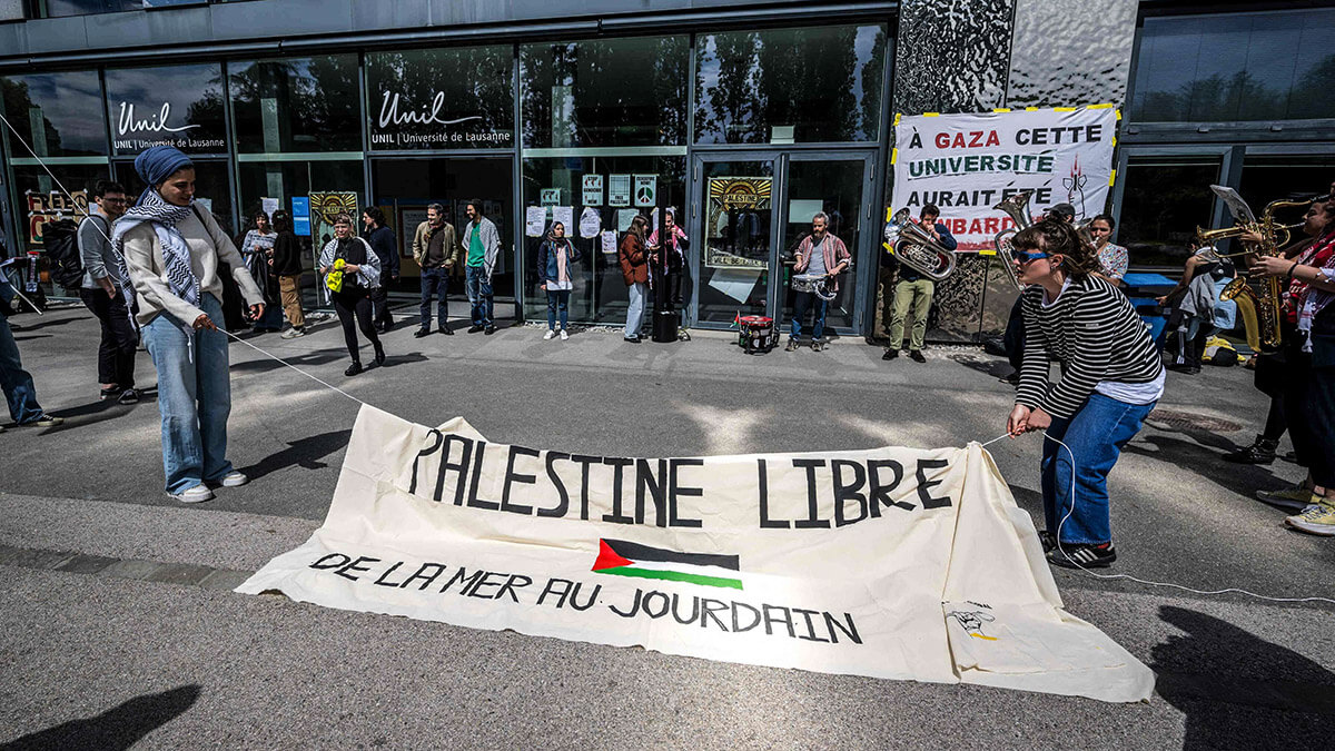 Estudiantes y activistas pro palestinos cuelgan una pancarta en francés que dice “Palestina libre desde el mar hasta el río Jordán”, durante una manifestación en la entrada del edificio Geopolis de la Universidad de Lausana (UNIL), ocupado por estudiantes pro palestinos, en Lausana el 4 de mayo de 2024 - AFP/FABRICE COFFRINI