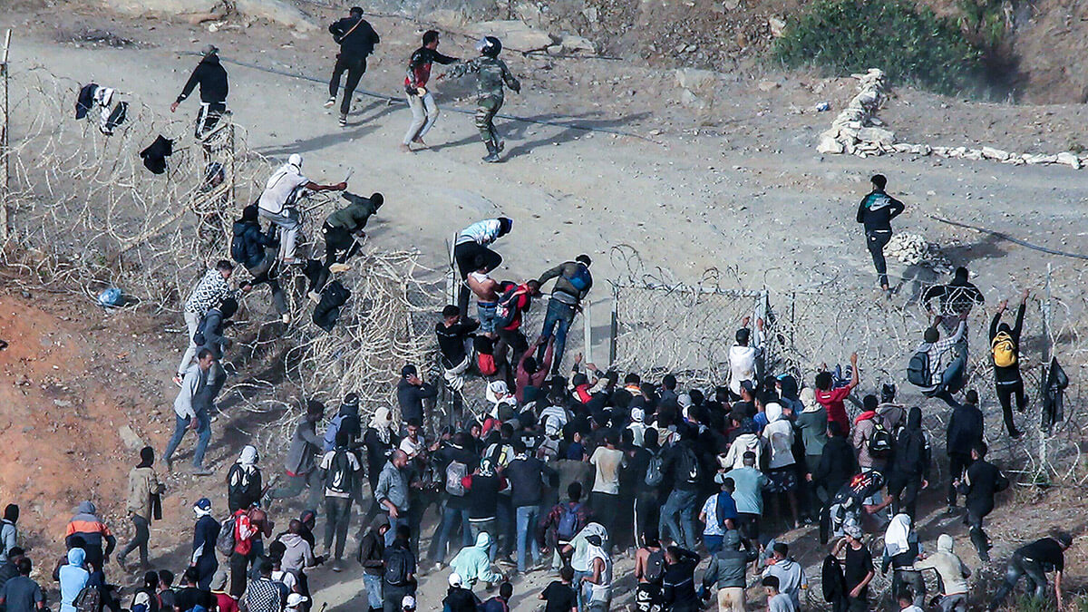 <p>Migrantes asaltan una valla de alambre de púas mientras intentan cruzar la frontera terrestre con el enclave africano de España, Ceuta, cerca de Fnideq, en el norte de Marruecos, el 15 de septiembre de 2024 - PHOTO/AFP</p>