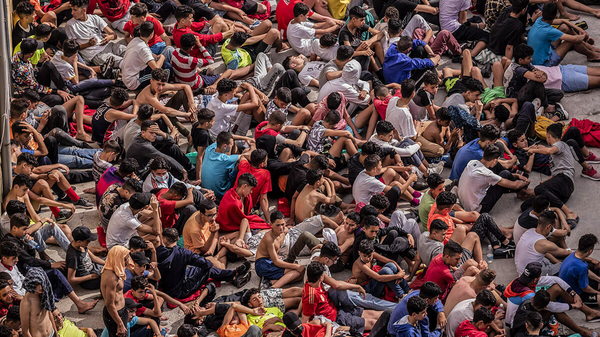 <p>En esta fotografía de archivo del 19 de mayo de 2021, menores no acompañados que cruzaron a España se reúnen afuera de un almacén utilizado como refugio temporal mientras esperan ser sometidos a una prueba de COVID-19 en el enclave español de Ceuta, cerca de la frontera entre Marruecos y España - AP/BERNAT ARMANQUE</p>