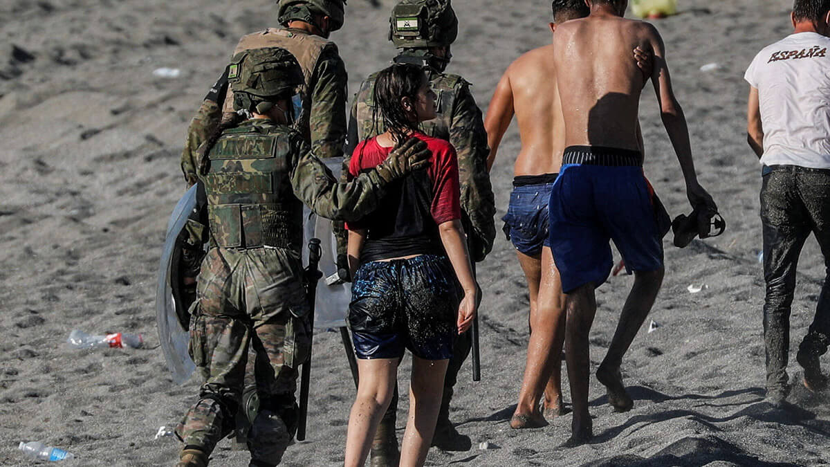 <p>Una mujer migrante es guiada por una soldado española mientras es deportada a Marruecos después de que cruzó la frontera nadando de Marruecos a España, en la playa de El Tarajal, después de que miles de migrantes nadaran a través de esta frontera durante los últimos días, en Ceuta, España, el 19 de mayo de 2021 - REUTERS/ JON NAZCA</p>