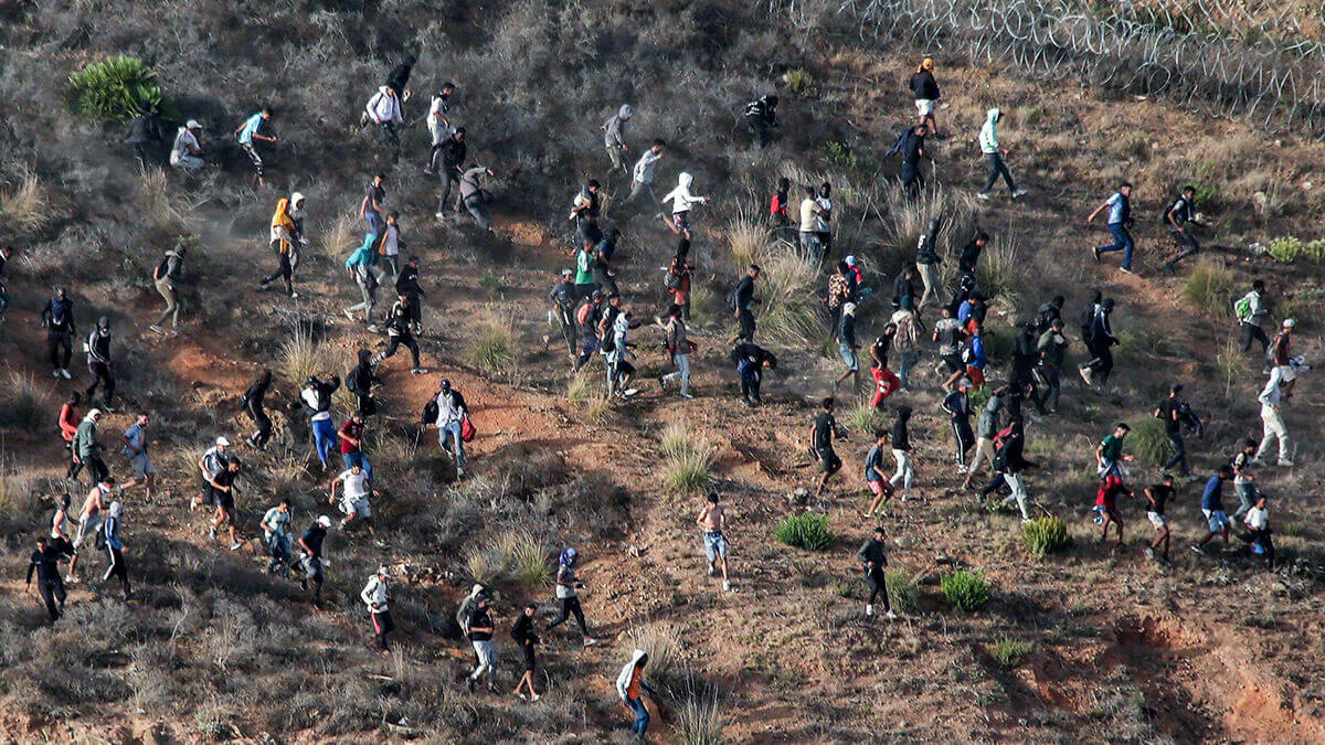 Los migrantes asaltan una valla de alambre de púas mientras intentan cruzar la frontera terrestre con el enclave africano de España, Ceuta - PHOTO/ AFP