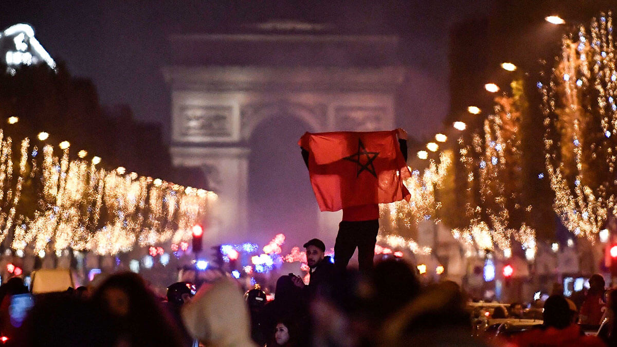 <p>Un hincha de Marruecos ondea una bandera nacional cerca del Arco de Triunfo, para celebrar la victoria de los equipos nacionales después del partido de fútbol de la Copa Mundial de Qatar 2022 entre Marruecos y España, en los Campos Elíseos en París el 6 de diciembre de 2022 - AFP/JULIEN DE ROSA </p>