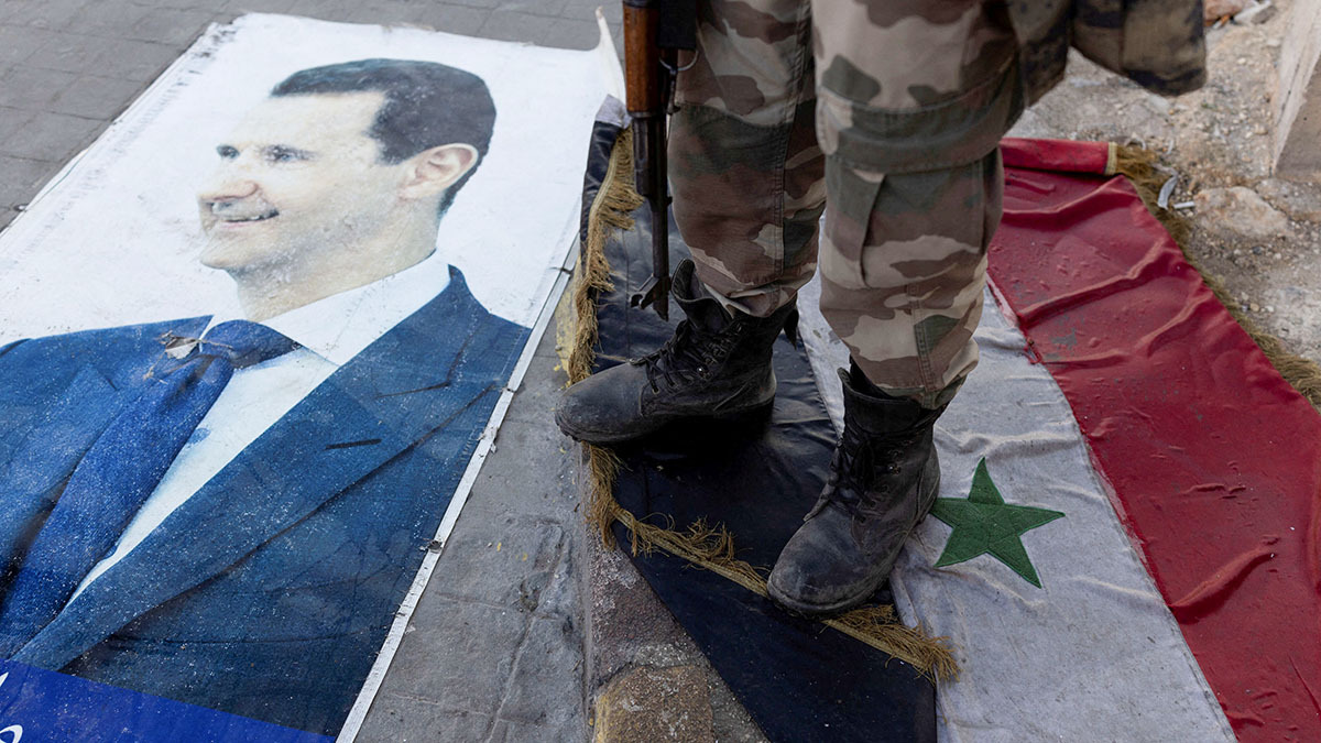 Un combatiente del partido gobernante sirio pisa una bandera siria bajo el régimen de Bashar al-Assad, tendida en el suelo junto a una foto del derrocado Bashar al-Assad, en Alepo, Siria - REUTERS/ UMIT BEKTAS