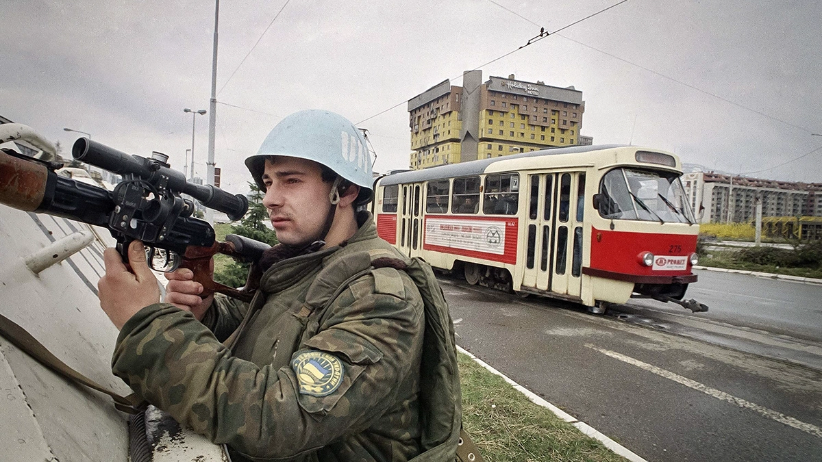 En esta fotografía de archivo del domingo 27 de marzo de 1994, un soldado ucraniano de la ONU sostiene un arma mientras protege un tranvía que atraviesa la llamada Avenida de los Francotiradores, en Sarajevo, Bosnia, con el hotel Holiday Inn como telón de fondo - AP/ENRIC MARTI